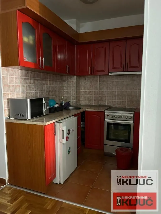 Small kitchen with red cabinets, stove, and refrigerator.