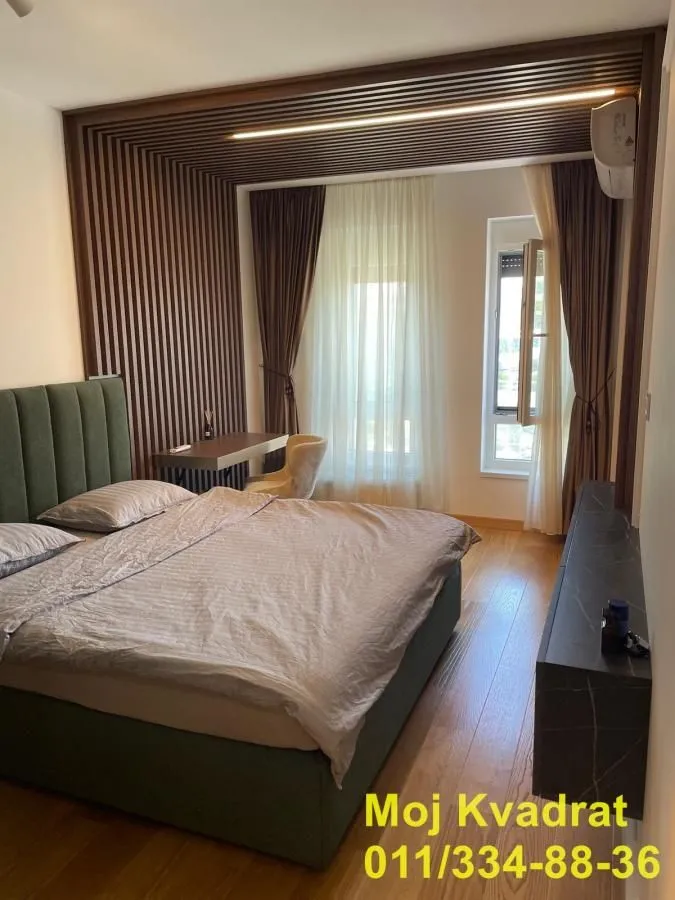 Moderna spavaća soba sa bračnim krevetom, drvenim zidnim panelima i radnim stolom.
