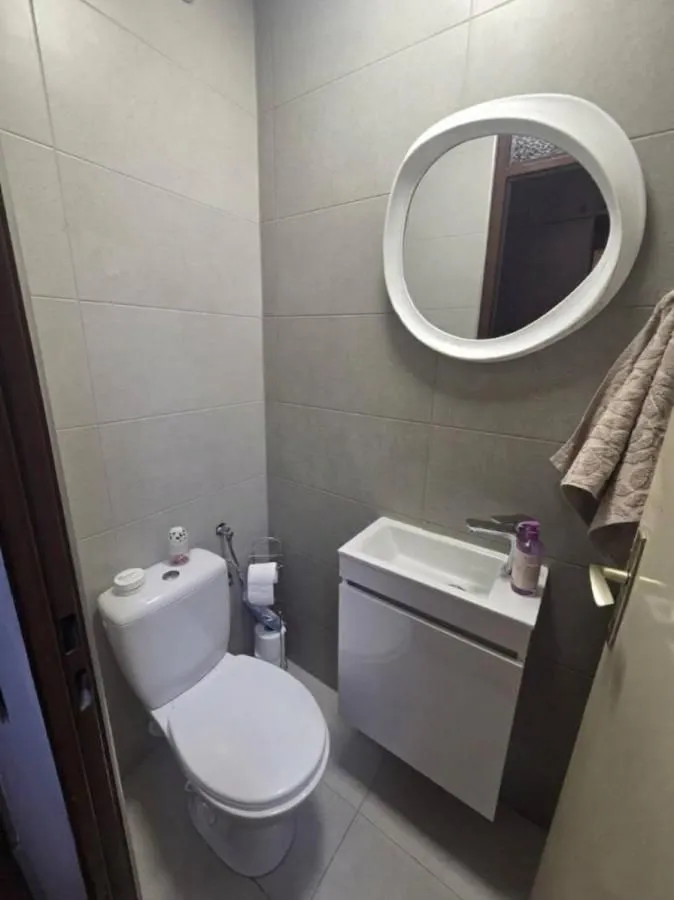 Manje kupatilo sa wc šoljom, umivaonikom i okruglim ogledalom.