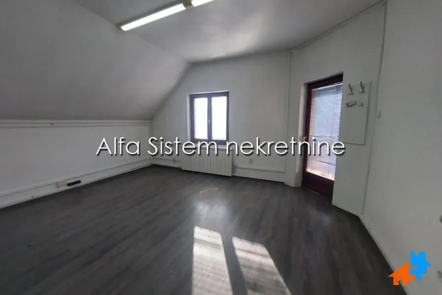An empty attic room with dark flooring, a window, and a door leading to a terrace.