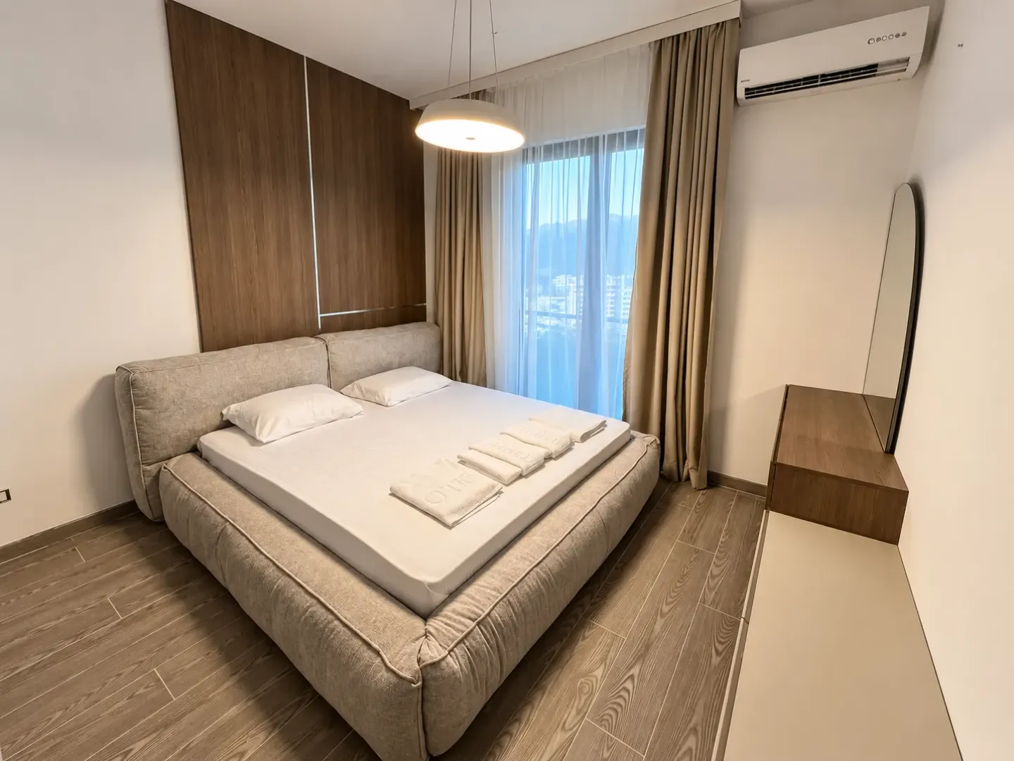 Modern bedroom with a double bed, wooden wall paneling, and a window with curtains.