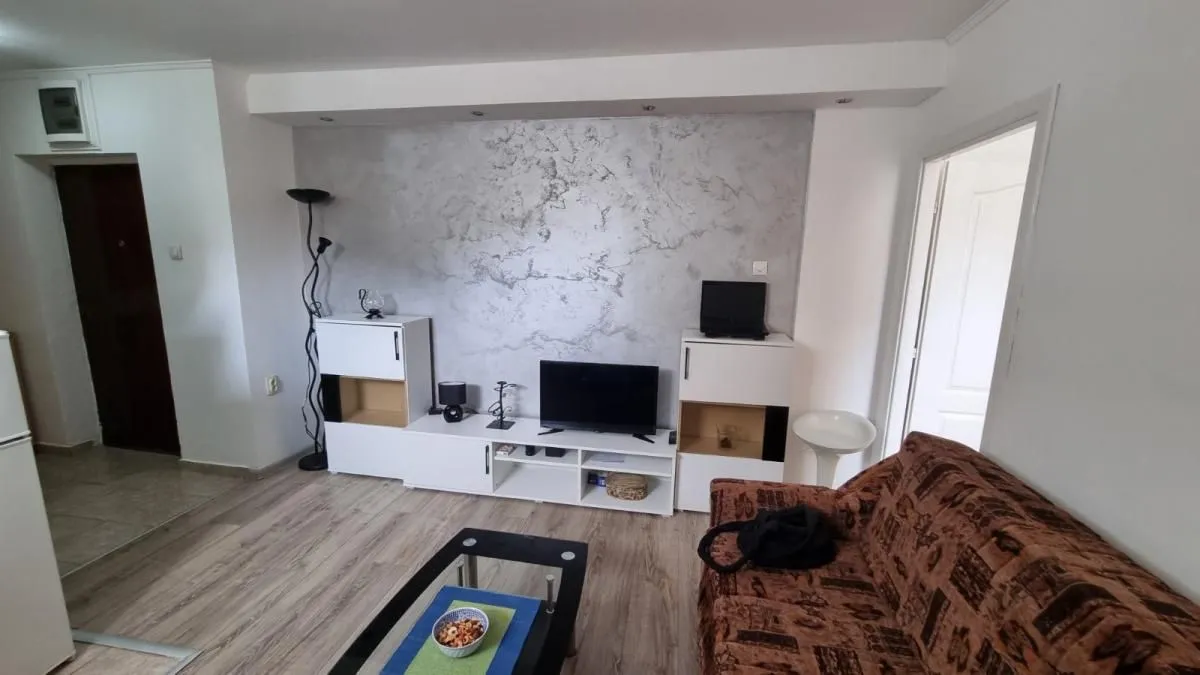 Dnevna soba sa garniturom, televizorom i belim komadnim nameštajem.