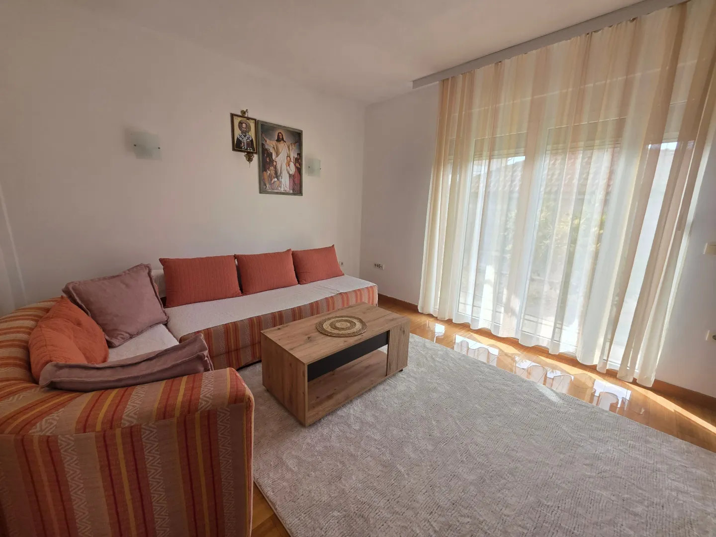 Living room with a sectional sofa, coffee table, and a large window with light curtains.