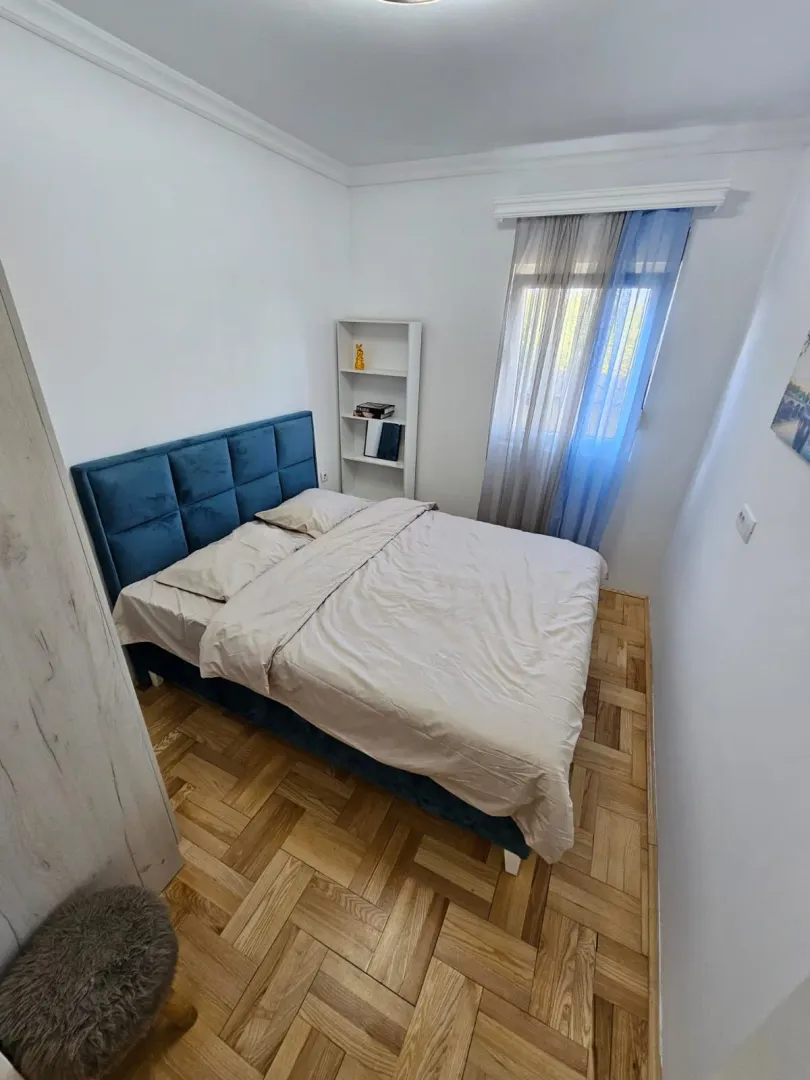 Manja spavaća soba sa bračnim krevetom, bijelom policom i prozorom.
