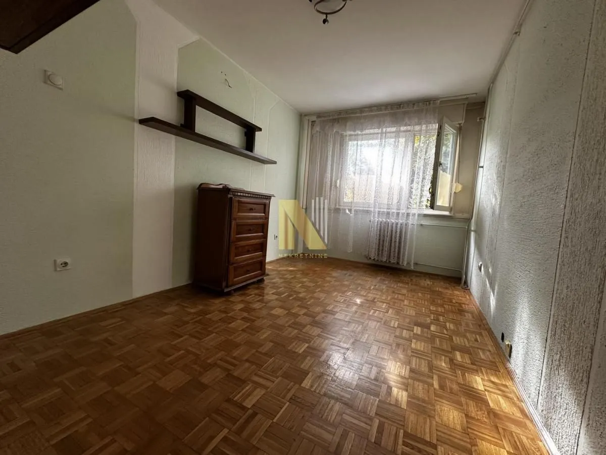 Prazna prostorija sa drvenim podom, komodom i policom na zidu.