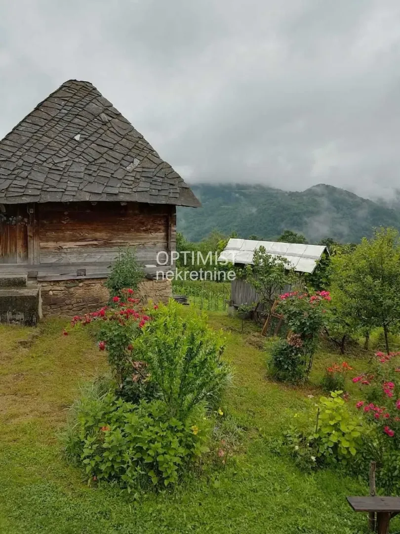 Tradicionalna drvena kuća u dvorištu sa pogledom na planine.