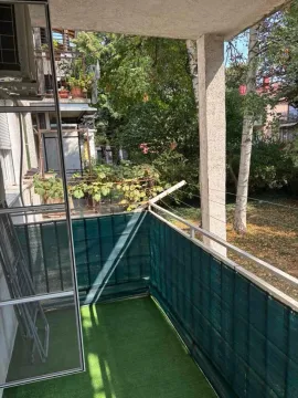 Covered balcony with a view of a green courtyard and trees. - image 5