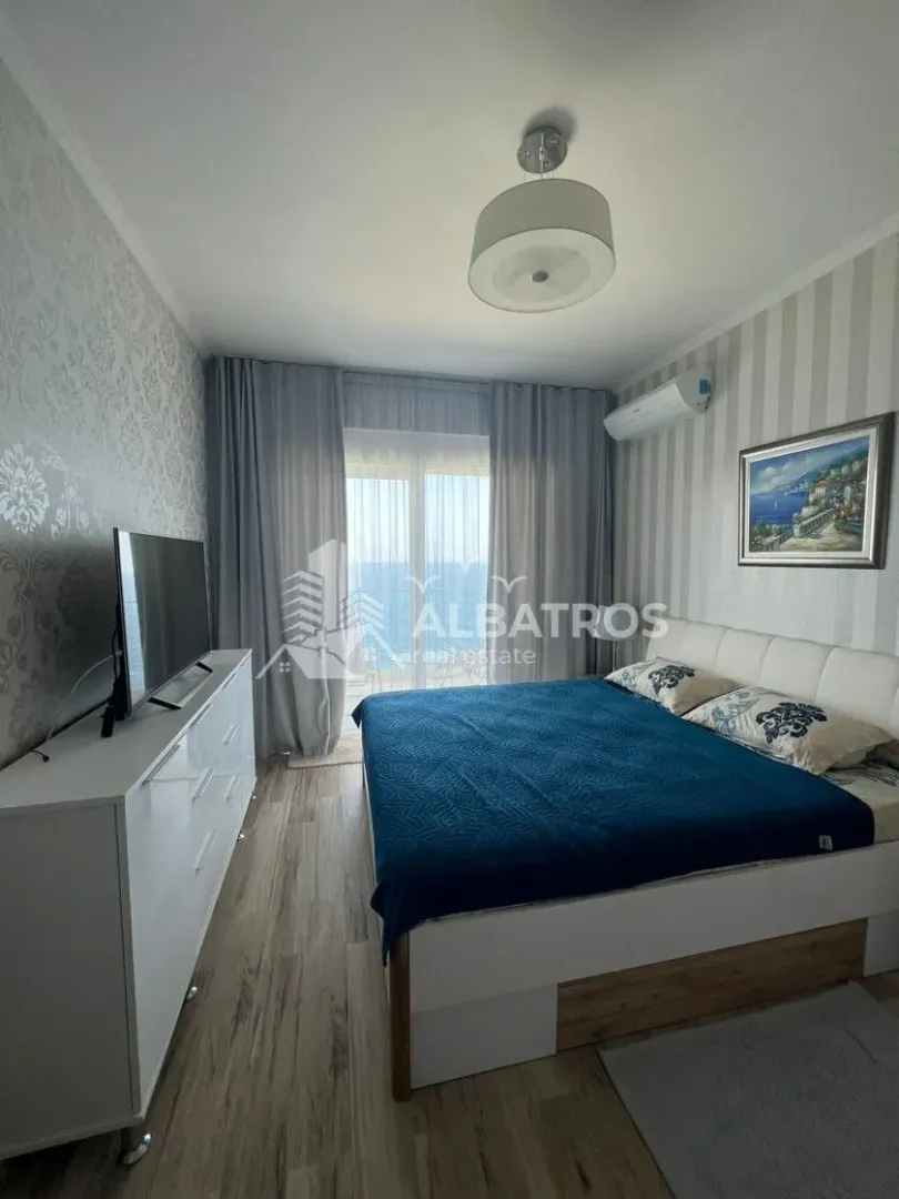 Namještena spavaća soba sa bračnim krevetom, komodom i izlazom na balkon sa pogledom na more.