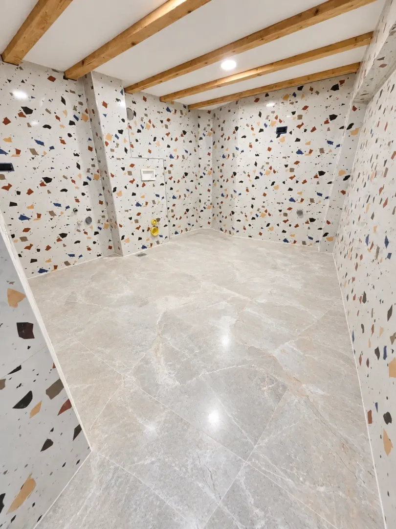 Empty bathroom with terrazzo tiles and wooden ceiling beams.