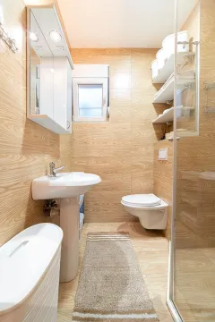 Bathroom lined with wood-textured ceramic tiles, featuring a sink, toilet, and shower cabin. - image 3