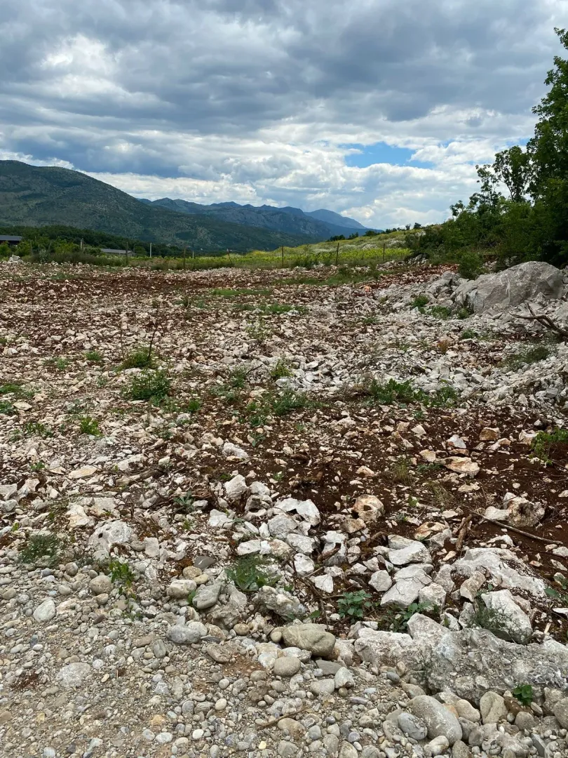 Pogled na neuređeni plac sa kamenim tlom i okolnim planinama u pozadini.