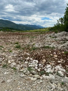 Pogled na neuređeni plac sa kamenim tlom i okolnim planinama u pozadini. - image 3