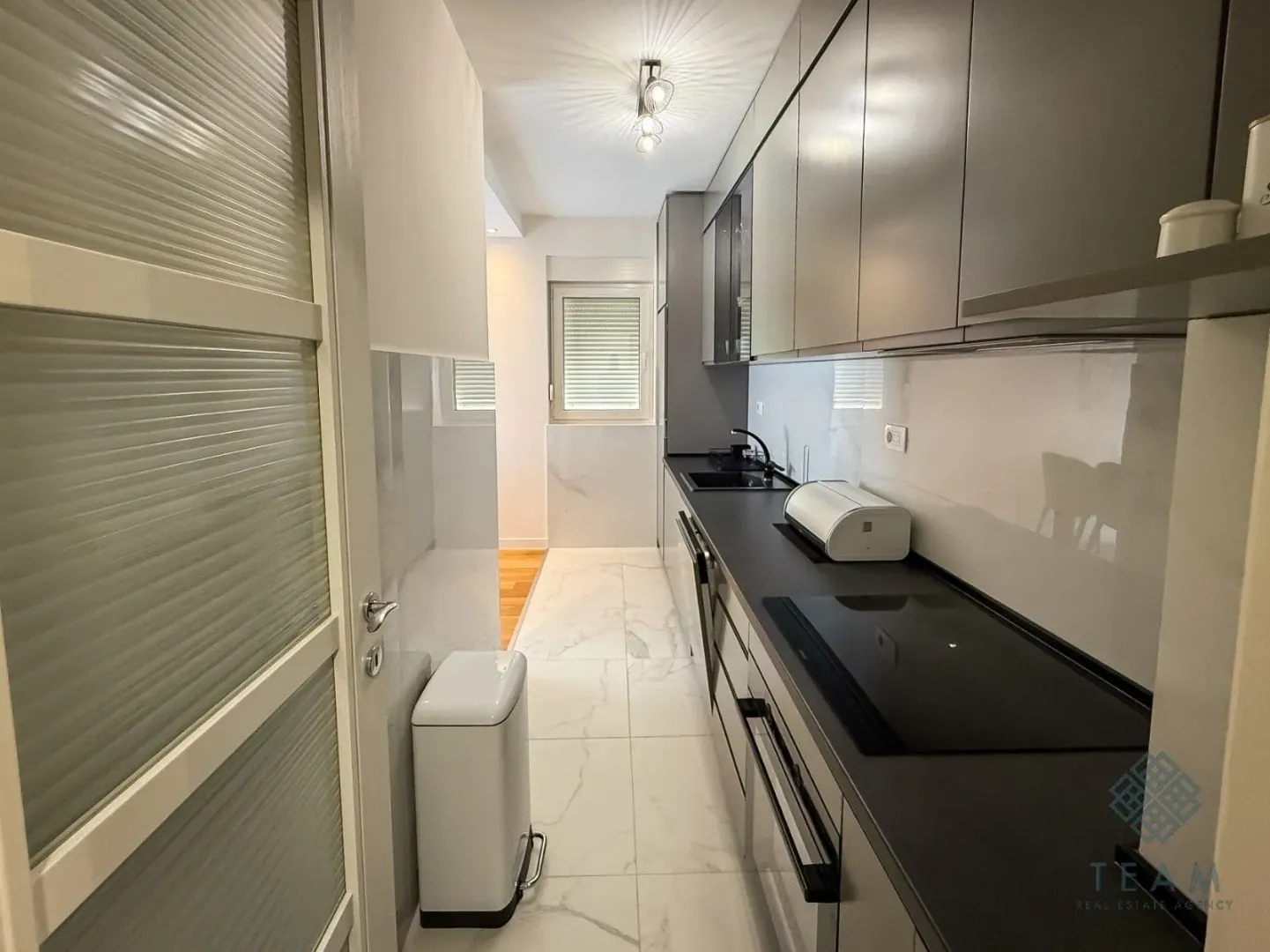 Modern narrow kitchen with dark cabinets and white floor tiles.