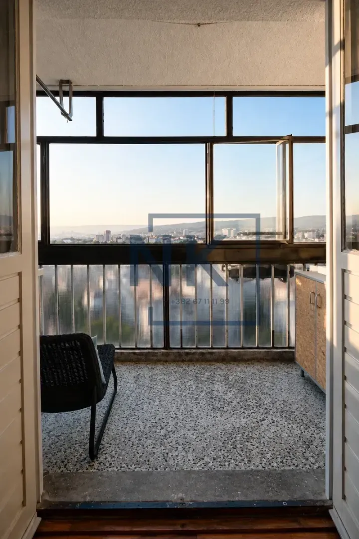 Zastakljeni balkon sa stolicom i pogledom na grad.