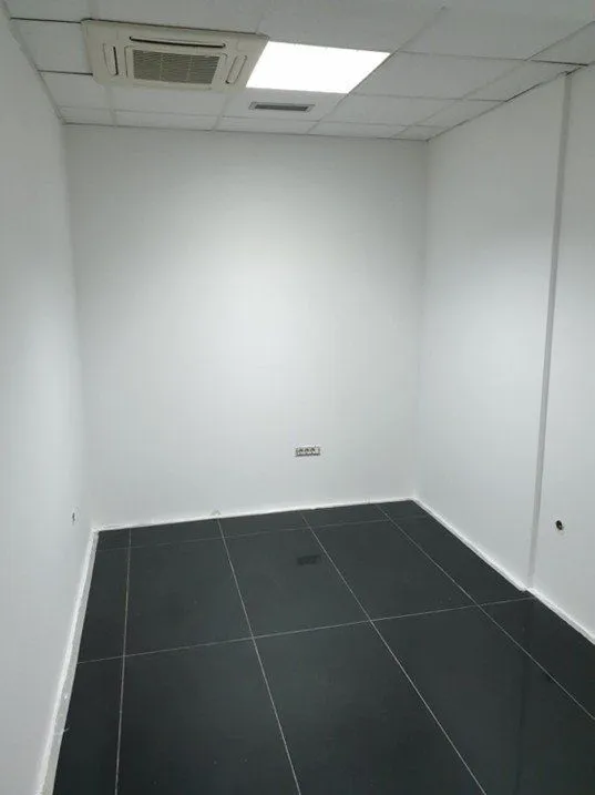 Empty office room with white walls and dark floor tiles.