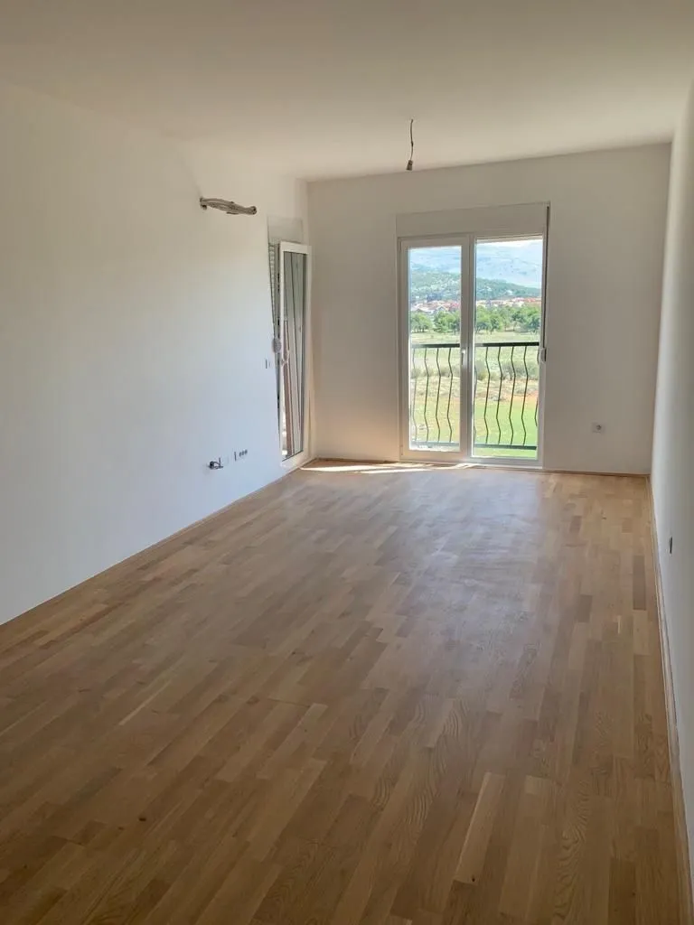 Prazna i svijetla soba sa novim parketom i izlazom na balkon.