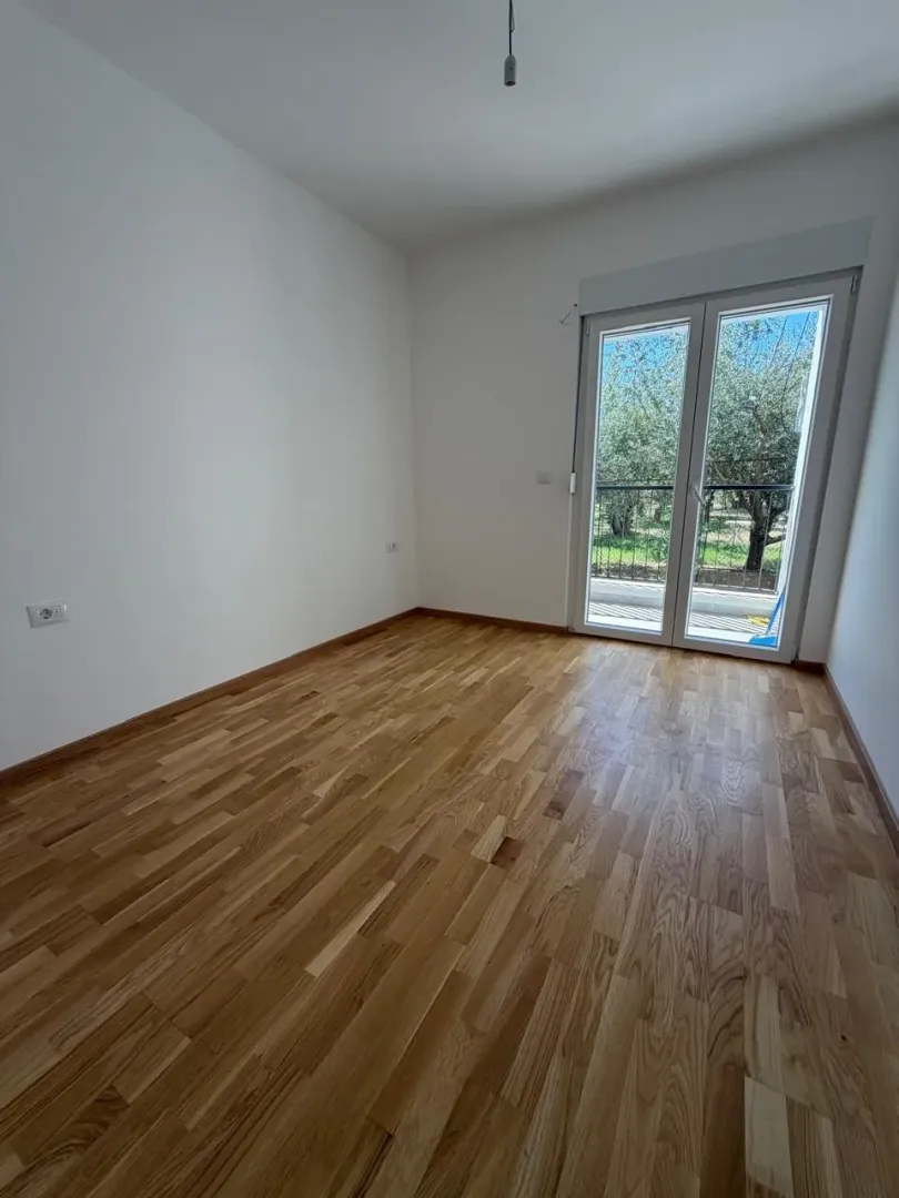 Prazna soba sa parketom i balkonskim vratima.