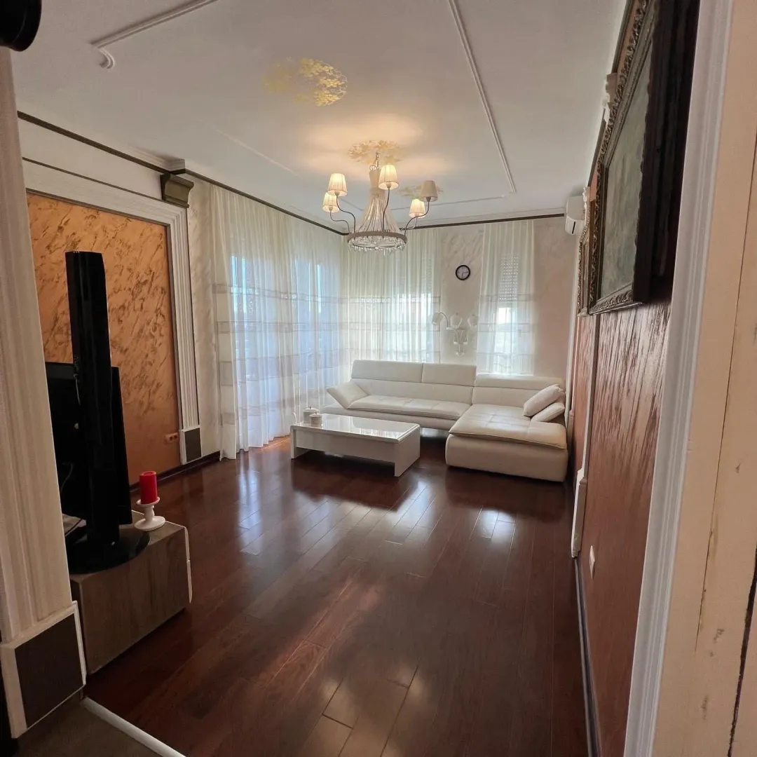 Spacious living room with a white sectional sofa and dark wooden flooring.