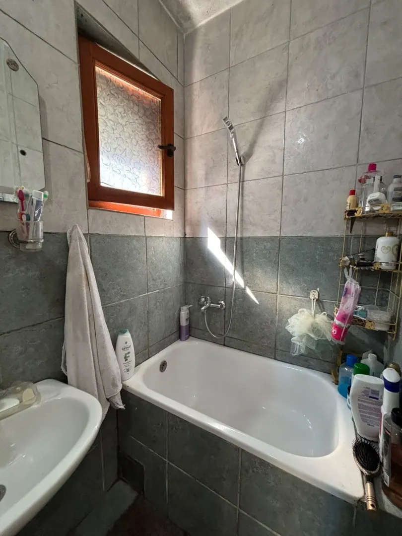 Small bathroom with a bathtub, washbasin, and a window, tiled with ceramic tiles.