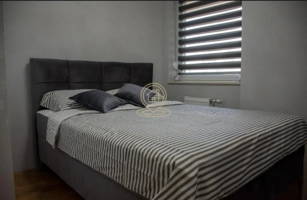 Spavaća soba sa velikim bračnim krevetom i prozorom sa roletnama.