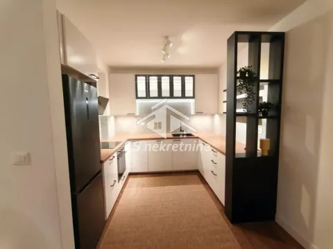 Moderna kuhinja sa belim elementima, drvenom radnom površinom i crnim frižiderom. - image 5