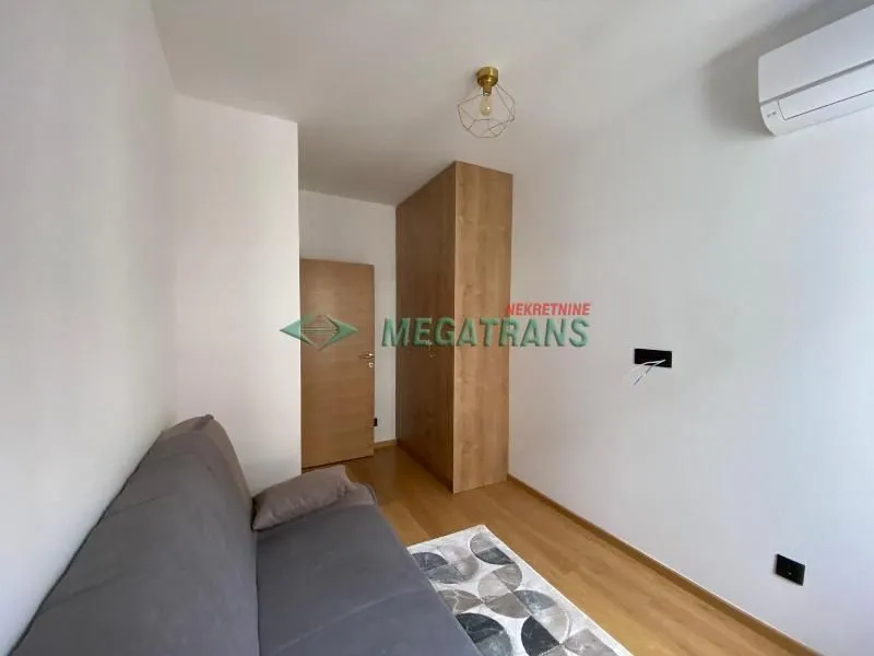 Living room with a grey sofa, wooden wardrobe, and air conditioning unit.