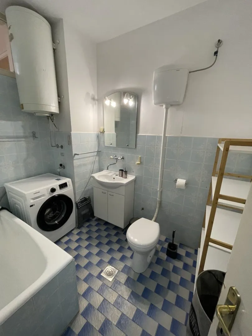 Jednostavno kupatilo sa veš mašinom, kadom i plavim pločicama.