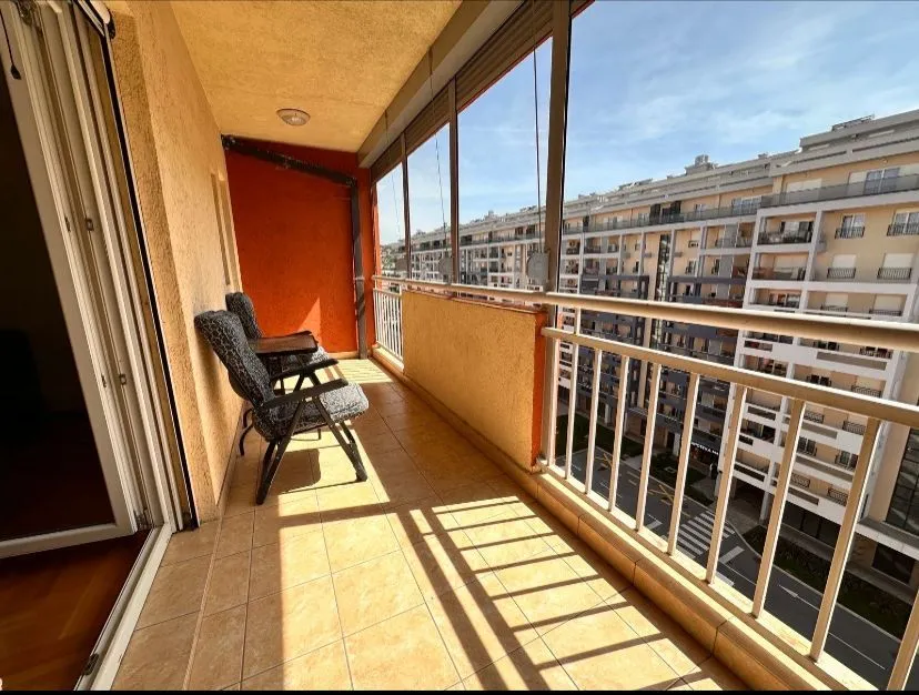 Natkriveni balkon sa staklenom ogradom i pogledom na okolne zgrade.