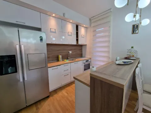 Modern kitchen with white cabinetry, large refrigerator, and a bar counter with dining chairs. - image 25