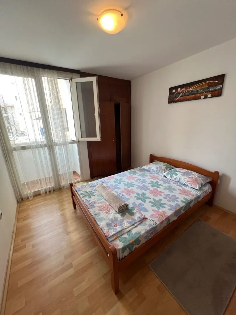 Spavaća soba sa bračnim krevetom, drvenim ormarom i izlazom na terasu.