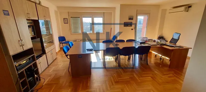 Prostrana prostorija opremljena kao kancelarija sa stolom za sastanke i drvenim regalima.