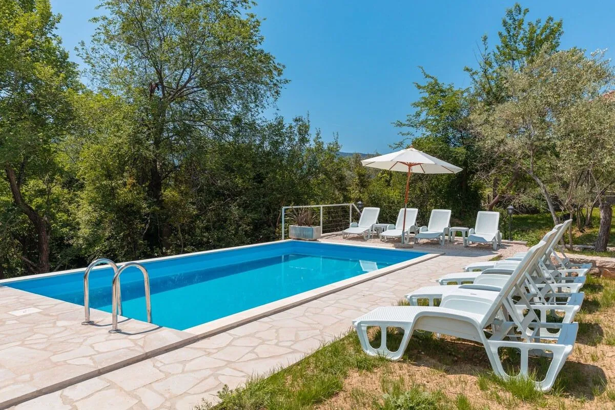 Outdoor area with a swimming pool and sun loungers surrounded by greenery.