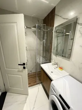 Bathroom with a shower cabin, washbasin, mirror, and washing machine. - image 6