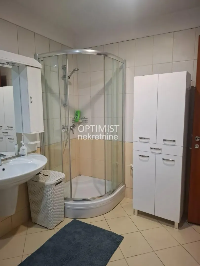Kupatilo opremljeno tuš kabinom, umivaonikom i belim kupatilskim ormarićem.