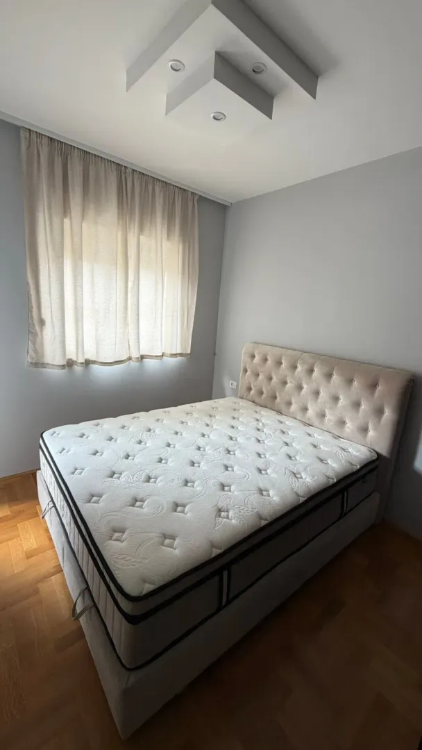 Bedroom with a double bed and a window covered by a curtain.