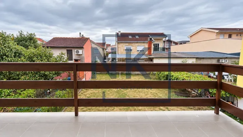 View of the yard and surrounding houses from the tiled balcony with a wooden railing.