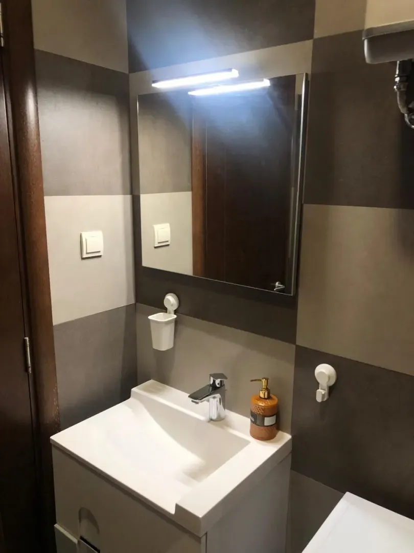 Small bathroom with a sink, mirror, and tiles in shades of grey.