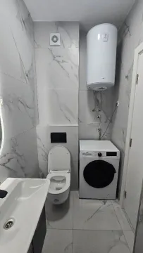 Modern bathroom with white tiles, toilet, washbasin, washing machine, and water heater. - image 2