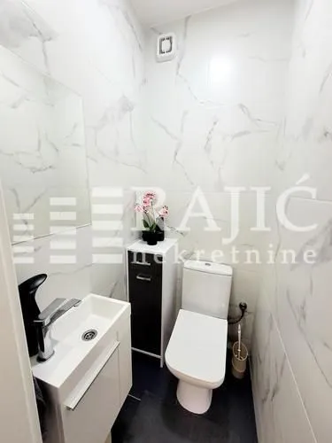 Smaller bathroom with white marble-textured ceramic tiles, a washbasin, and a toilet bowl.