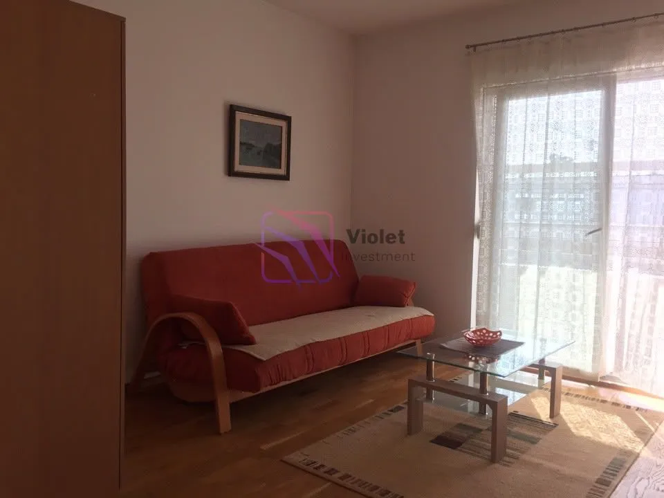Dnevna soba sa crvenim kaučem, staklenim stočićem i izlazom na terasu.