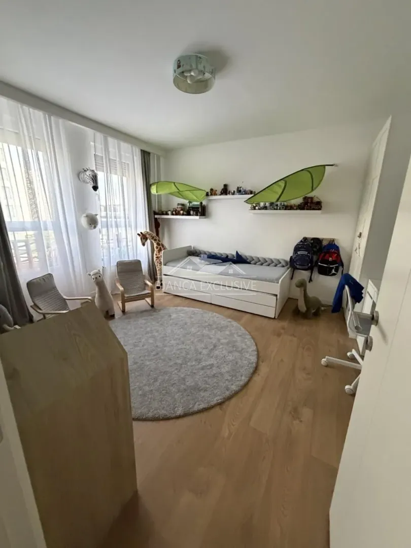 Dečja soba sa krevetom, radnim stolom i velikim prozorima.
