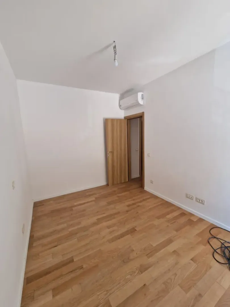 Empty room with white walls, wooden flooring, and an air conditioning unit.