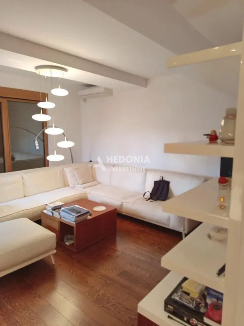 Dnevna soba sa ugaonom garniturom, drvenim stočićem i modernim lusterom.