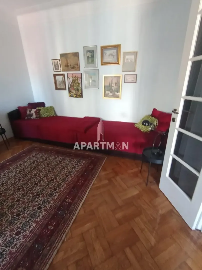 Dnevna soba sa crvenom garniturom, tepihom i slikama na zidu.