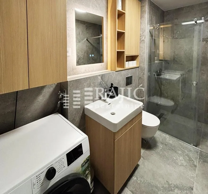 Modernly equipped bathroom with a shower cabin, sink, and washing machine.