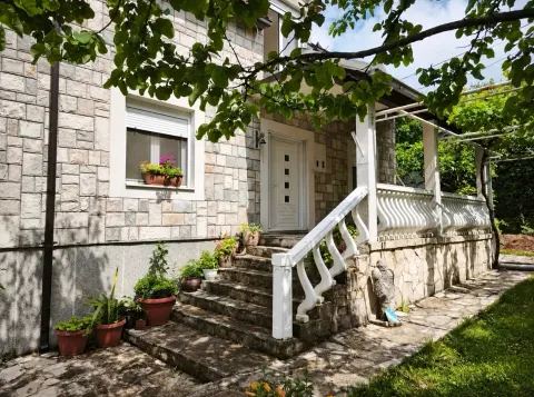 Fasada kuće sa kamenim oblogama, ulaznim stepeništem i trijemom okruženim zelenilom. - image 4