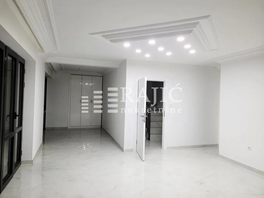 Empty bright room with marble flooring and a drop ceiling with recessed lighting.