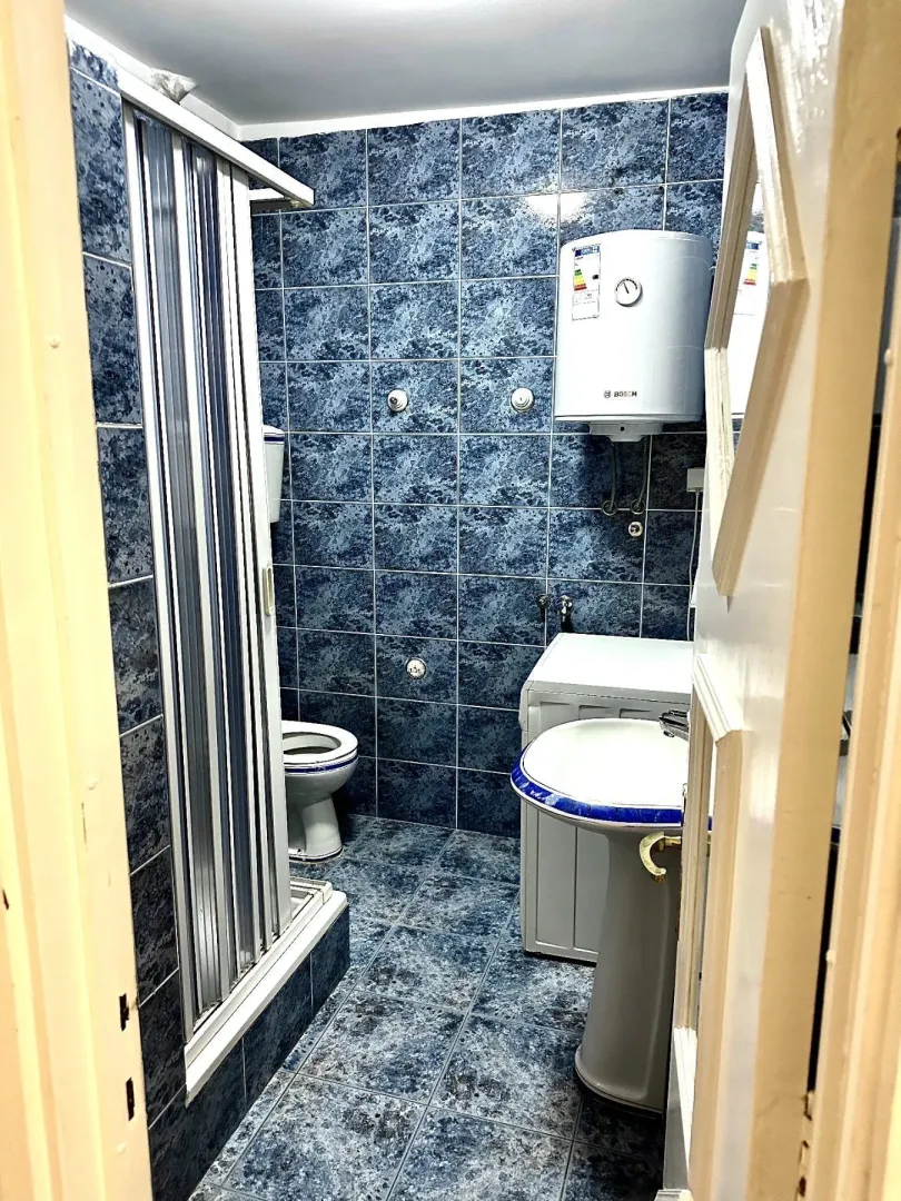 Kupatilo sa plavim pločicama, tuš kabinom i veš mašinom.