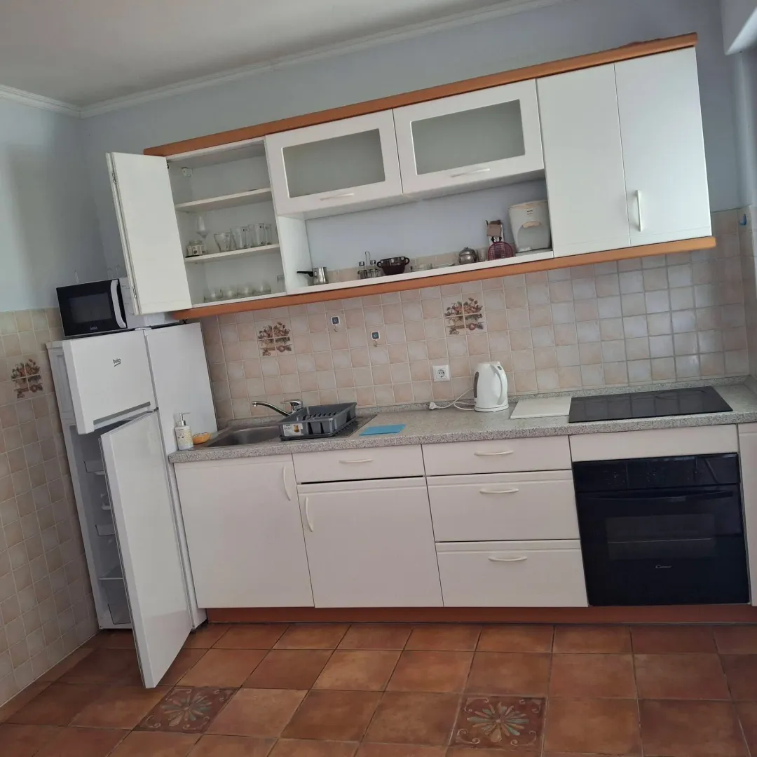 Manja opremljena kuhinja sa bijelim elementima i otvorenim vratima frižidera i gornjeg elementa.