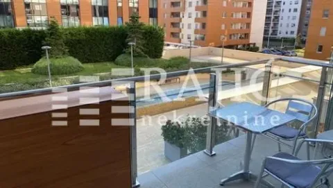 Manji namešten balkon sa stolom i stolicama i pogledom na uređeno dvorište i zgrade. - image 7